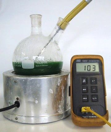A flask of green 50/50 water and glycol coolant boiling on the same hotplate, the thermometer reading 103°C