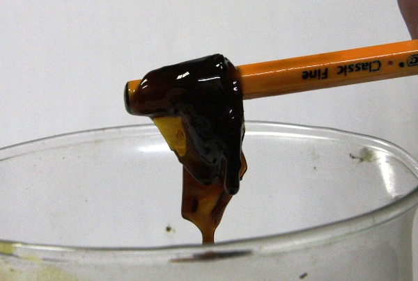 Dark, stringy, mucus-like biofilm lifted out of a jar of diesel on a pencil