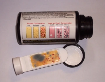 The test kit's black container, with the comparison chart printed on its side, beside a dip slide showing contamination