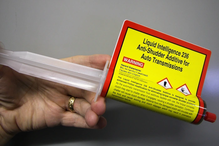 A hand holding the Liquid Intelligence 236 Anti-Shudder Additive syringe