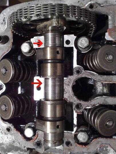 A camshaft in an open cylinder head, with arrows to badly worn lobes