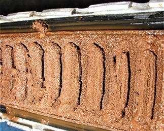 A radiator core cut open after a traditional stop leak: its flutes almost entirely blocked by wet, bloated cellulose particles