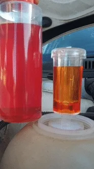 The leak tester seated in a vehicle's expansion bottle, its test fluid turned yellow beside a bottle of the red test fluid