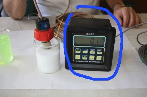 A conductivity meter reading 0.1 mS/cm with its probe in a beaker of milky 600 coolant
